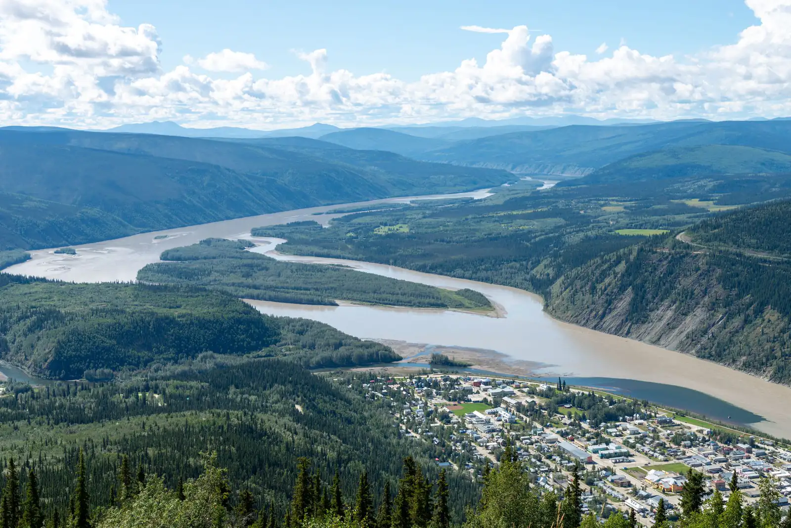 Dawson City beside the Yukon River seen from a forested hilltop